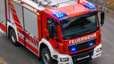 KI-generiertes Bild: Ein rotes Feuerwehrfahrzeug mit Blaulicht auf einer Straße.