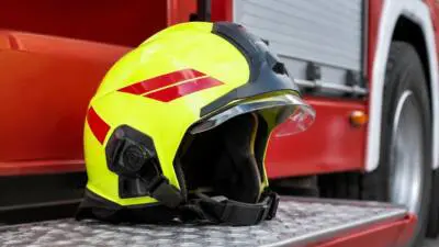 KI-generiertes Bild: Ein gelber Schutzhelm liegt auf einer Metalltrittfläche vor einem roten Fahrzeug.