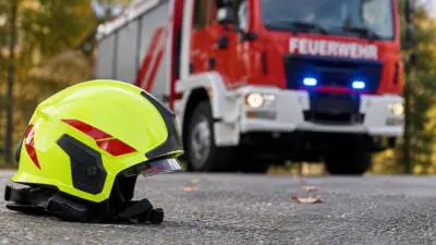 KI-Symbolbild: Ein Feuerwehrhelm liegt vor einem roten Feuerwehrfahrzeug.