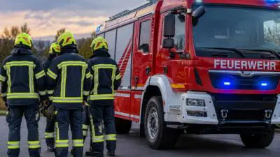 KI-generiertes Bild: Feuerwehrleute stehen neben einem roten Feuerwehrfahrzeug.
