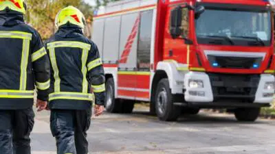 KI-generiertes Bild: Personen in dunkler Schutzkleidung mit gelben Helmen vor einem roten Einsatzfahrzeug.