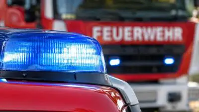 KI-Symbolbild: Blaues Kennlicht auf rotem Einsatzfahrzeug vor einem Feuerwehrfahrzeug.
