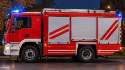 KI-Symbolbild: Rotes Einsatzfahrzeug mit Blaulicht auf einer Straße bei Nacht.
