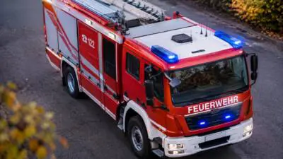 KI-Symbolbild: Ein rotes Feuerwehrfahrzeug mit Dachleitern steht auf einer Straße.