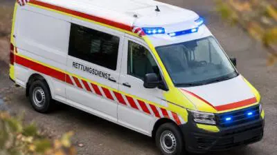 KI-generiertes Bild: Ein weißer Rettungswagen mit rot-gelben Streifen und eingeschaltetem Blaulicht.