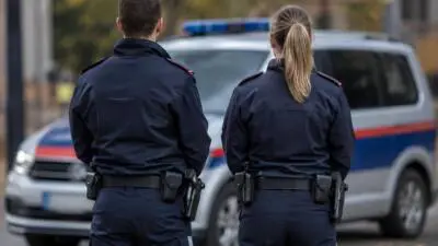 KI-Symbolbild: Uniformierte Personen stehen vor einem weißen Fahrzeug mit blau-roten Streifen.