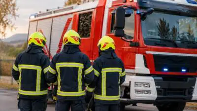 KI-Symbolbild: Personen in dunkler Schutzkleidung vor einem roten Feuerwehrfahrzeug.