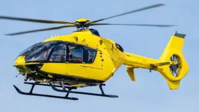 KI-Symbolbild: Ein gelber Hubschrauber fliegt vor blauem Himmel.