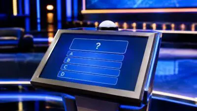 Ein beleuchtetes Quizpult mit Fragezeichen und Antwortoptionen auf einer blauen Studiobühne
