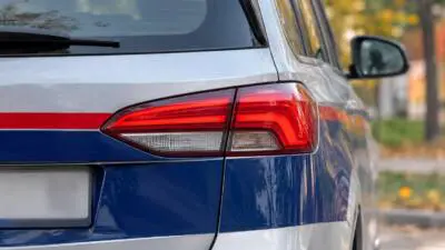 KI-Symbolbild: Nahaufnahme des Hecks eines silber-blauen Autos mit roter Rückleuchte.