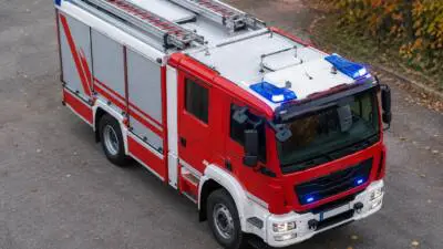 KI-Symbolbild: Ein rotes Einsatzfahrzeug mit Leiteraufbau steht auf einer Straße.
