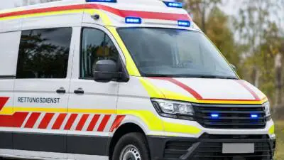 KI-generiertes Bild: Weißer Rettungswagen mit roten und gelben Streifen und Blaulicht.