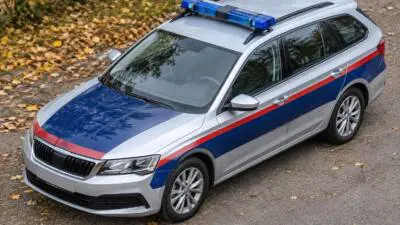 KI-Symbolbild: Ein silberner Kombi mit blauem Blaulicht und rot-blauer Beklebung steht auf einem herbstlichen Weg.