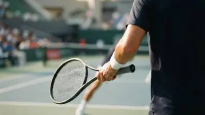 KI-generiertes Bild: Eine Person in dunkler Sportkleidung hält einen Tennisschläger auf einem Tennisplatz.