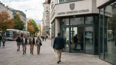 KI-Symbolbild: Menschen gehen an einem modernen Gebäude mit Glaseingang vorbei, links ist eine Straßenbahn zu sehen.