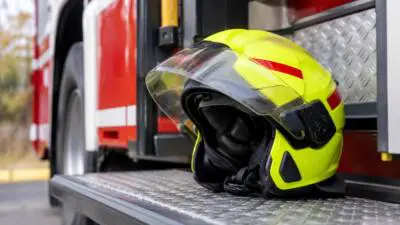 KI-Symbolbild: Ein neongelber Schutzhelm liegt auf einer Metallstufe vor einem rot-weißen Fahrzeug.