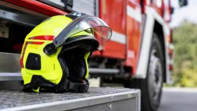 KI-generiertes Bild: Ein leuchtgelber Helm liegt auf einer Trittfläche vor einem roten Einsatzfahrzeug.