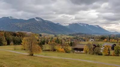 KI-generiertes Bild: Herbstliche Berglandschaft mit Häusern, Feldern und dicht bewölktem Himmel