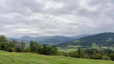 KI-generiertes Bild: Bewölkter Himmel über grünen Wiesen und bewaldeten Hügeln.