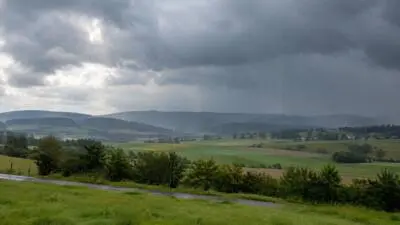 KI-Symbolbild: Dunkle Wolken und Regen über grünen Feldern und Hügeln.