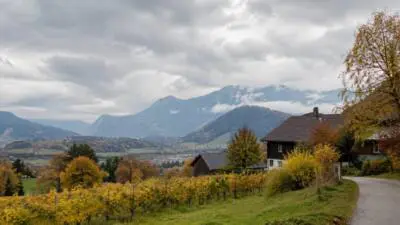 KI-generiertes Bild: Wolken über einem herbstlichen Tal mit Bergen, Wiesen und Häusern.
