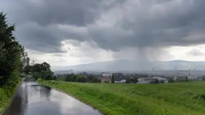 KI-Symbolbild: Dunkle Regenwolken über einer Stadt und Regen in der Ferne.