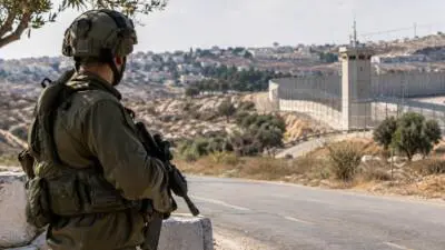 KI-Symbolbild: Ein bewaffneter Soldat steht an einer Straße vor einer Sperranlage.
