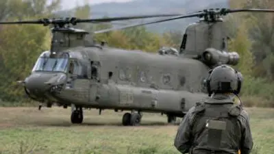 KI-generiertes Bild: Ein olivgrüner Transporthubschrauber steht auf einer Wiese, davor ein Soldat mit Helm.