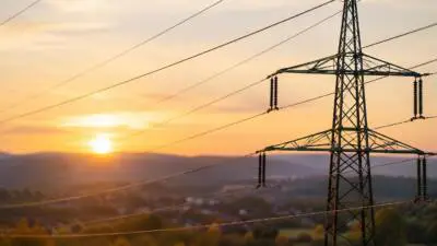 KI-generiertes Bild: Ein Hochspannungsmast mit Stromleitungen vor einer Landschaft im Abendlicht.