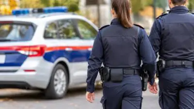 KI-Symbolbild: Uniformierte Personen neben einem weiß-blau-roten Fahrzeug mit Blaulicht.