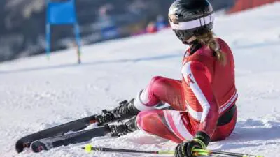 KI-Symbolbild: Eine Skifahrerin in rotem Rennanzug sitzt mit Skiern auf einer verschneiten Piste.