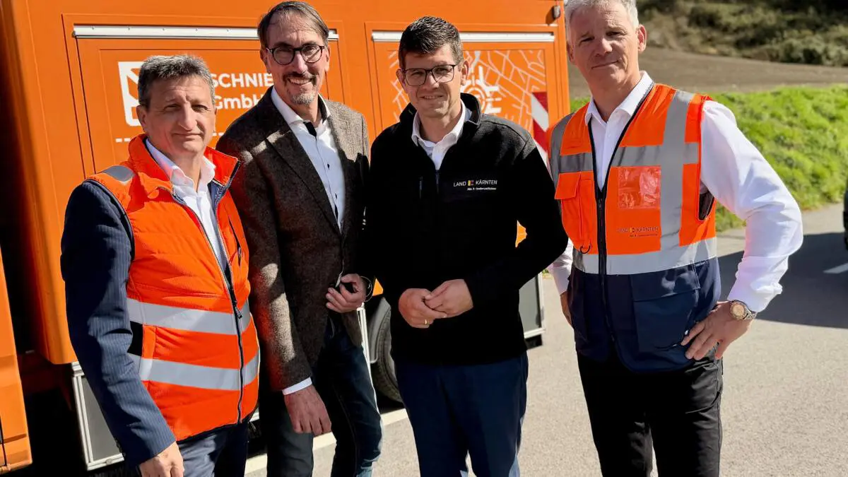 Männer in Warnwesten und Arbeitskleidung stehen vor einem orangefarbenen Fahrzeug.