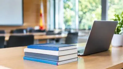 KI-generiertes Bild: Ein geöffneter Laptop und gestapelte Bücher stehen auf einem Tisch.