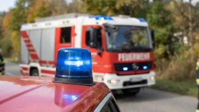 KI-Symbolbild: Eine blaue Rundumleuchte auf einem roten Fahrzeug, dahinter ein rot-weißes Feuerwehrfahrzeug.