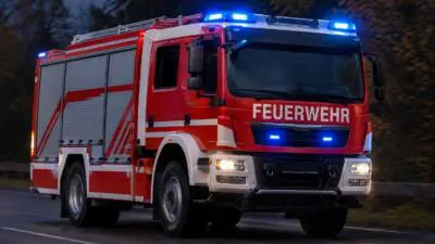 KI-generiertes Bild: Ein roter Feuerwehr-Lkw mit eingeschaltetem Blaulicht auf einer Straße.