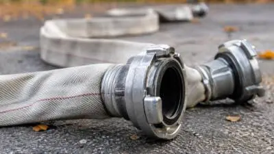 KI-Symbolbild: Ein heller Feuerwehrschlauch mit silbernen Kupplungen liegt auf Asphalt.
