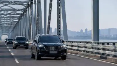 KI-Symbolbild: Dunkle Autos fahren über eine Stahlbrücke mit Blick auf einen Fluss.