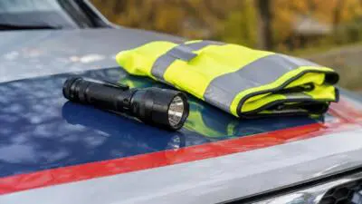 KI-generiertes Bild: Eine Warnweste und eine Taschenlampe liegen auf der markierten Motorhaube eines Autos.