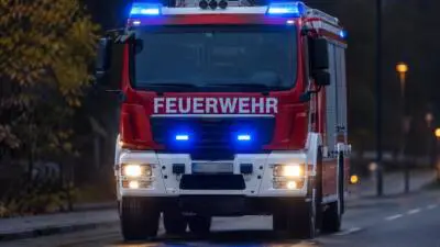 KI-Symbolbild: Ein rotes und weißes Feuerwehrfahrzeug mit eingeschaltetem Blaulicht auf einer Straße.