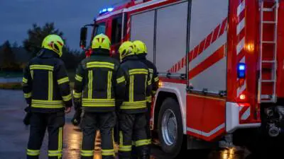 KI-Symbolbild: Personen in Schutzkleidung stehen neben einem roten Einsatzfahrzeug.