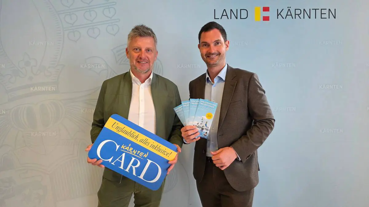 Zwei Männer präsentieren eine Kärnten-Card-Tafel und Folder zum Winterfreizeitpass.
