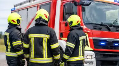 KI-generiertes Bild: Feuerwehrleute in Schutzkleidung stehen vor einem roten Einsatzfahrzeug.