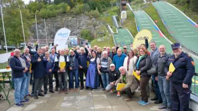 Gruppe von Erwachsenen vor Skisprungschanzen, einige halten gelbe Mappen.