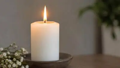 KI-generiertes Bild: Eine brennende weiße Kerze steht neben kleinen weißen Blüten.