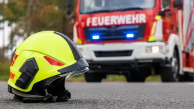 KI-generiertes Bild: Ein gelber Feuerwehrhelm vor einem roten Feuerwehrfahrzeug.