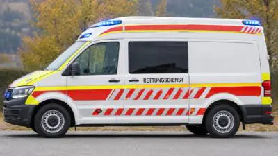 KI-generiertes Bild: Ein weißer Rettungswagen mit rot-gelben Streifen steht auf einer Straße.