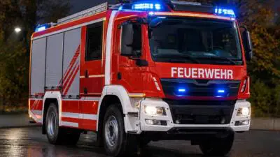 KI-generiertes Bild: Ein rotes Feuerwehrfahrzeug steht mit eingeschaltetem Blaulicht auf nasser Straße.