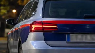 KI-Symbolbild: Heckansicht eines weiß-blauen Autos mit roten Streifen bei Nacht.