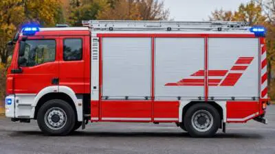 KI-Symbolbild: Ein rotes Einsatzfahrzeug mit silbernem Aufbau vor herbstlich gefärbten Bäumen.