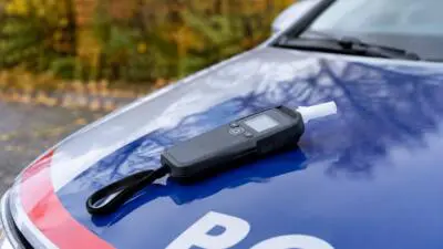 KI-generiertes Bild: Ein schwarzes Messgerät mit Mundstück liegt auf der Motorhaube eines blau-weißen Autos.